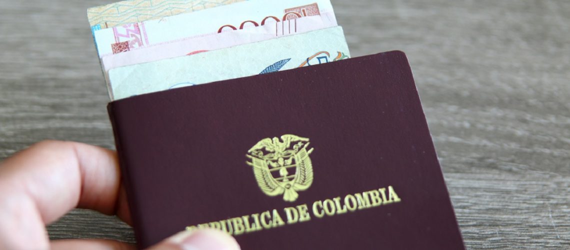 Colombian passport with bank notes over a light grey wooden background