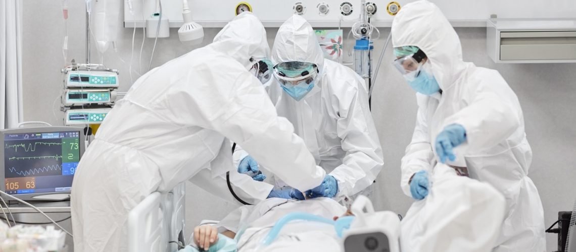 Male and female healthcare workers wearing full protective workwear providing emergency ventilator care to female patient having difficulty breathing.